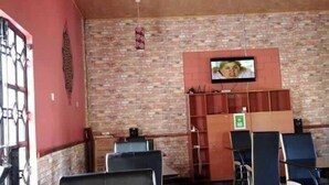 A restaurant interior with brick walls, a tiled floor, and a television mounted on the wall. - Acacia Shade Hotel and Gardens (Mutomo)