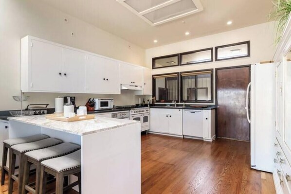 Une cuisine moderne avec des meubles blancs, un îlot central doté de tabourets, un four à micro-ondes, une cuisinière et un réfrigérateur.