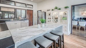 A modern kitchen with a marble island, bar stools, and a cabinet labeled "EAT".