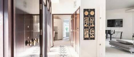 A modern interior with a hallway leading to a living area, featuring a patterned floor, a sofa, and a flat-screen TV.