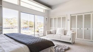 A bedroom with a large bed, a white sofa, and a view of a mountainous landscape through large windows.