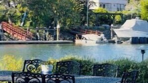 A lakeside patio with metal chairs and tables, a small bridge, and a boat dock.