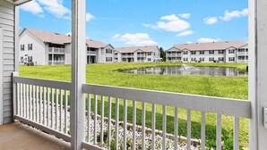 A view of a residential building complex with multiple two-story houses, a small pond, and a white fence.