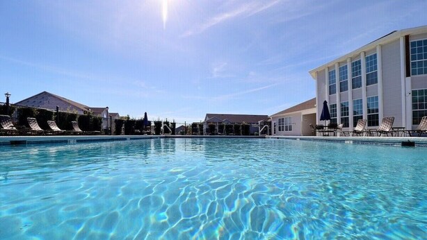 A clear swimming pool with lounge chairs and umbrellas, surrounded by buildings with large windows.