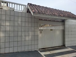 Uma entrada protegida por grades com um muro revestido de azulejos, um portão de metal e um telhado em telhas.