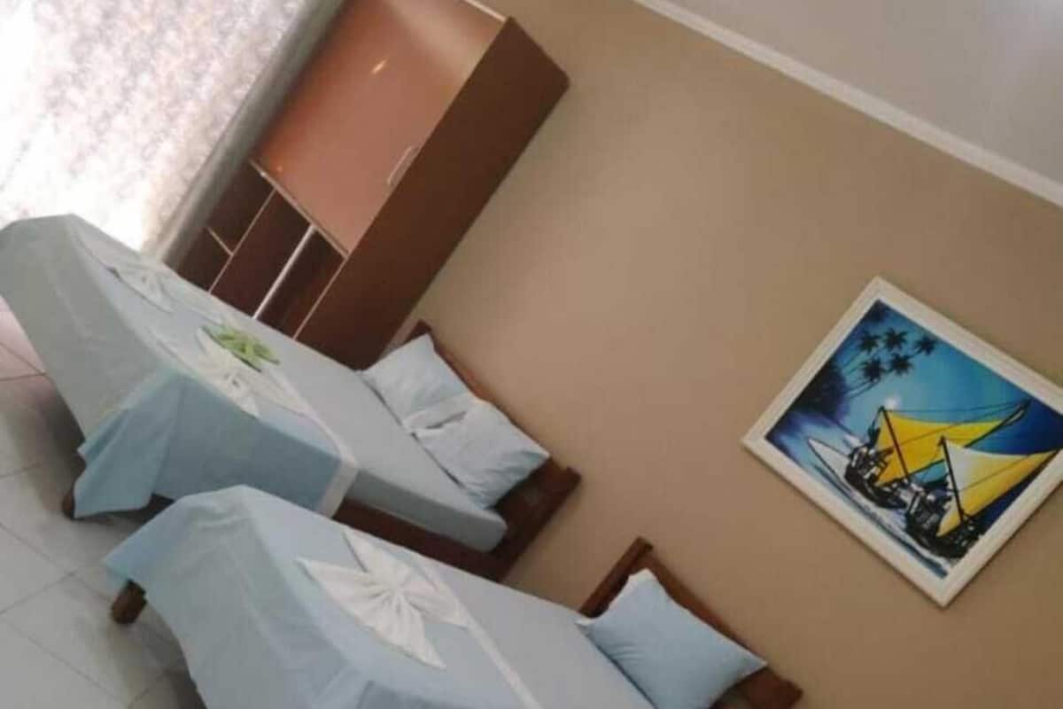 Una habitación de hotel con tres camas individuales, un armario y un cuadro en la pared.