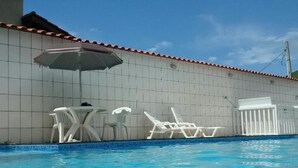 A swimming pool with white lounge chairs and a table, and a tiled wall with a red roof. - Suites Ubatuba Praia da Lagoinha (Ubatuba)