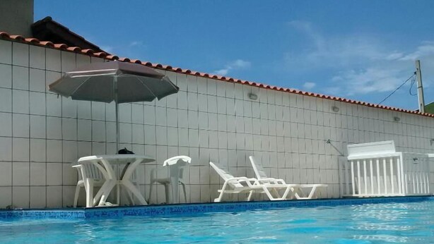 Una piscina con sillas de descanso blancas y una mesa, junto a una pared de azulejos con techo rojo.