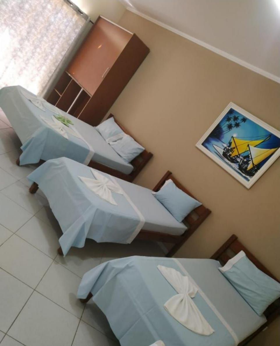 A hotel room with three single beds, a wardrobe, and a painting on the wall.