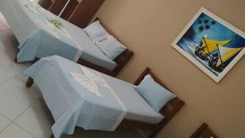 A hotel room with three single beds, a wardrobe, and a painting on the wall.