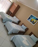 Quarto de hotel com três camas de solteiro, um guarda-roupa e um quadro na parede.