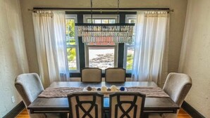 Un comedor con mesa de madera, cuatro sillas tapizadas y vistas a un patio de piedra a través de una ventana con cortinas.