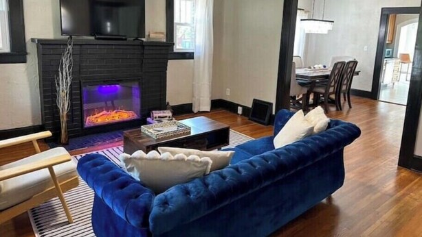 Una sala de estar con chimenea, un sofá azul, una mesa de centro de madera y un televisor montado sobre la chimenea.
