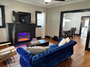 A living room with a fireplace, a blue sofa, a wooden coffee table, and a television mounted above the fireplace. - Hello Sunshine! Beautiful bungalow in the heart of Springfield! (Springfield)