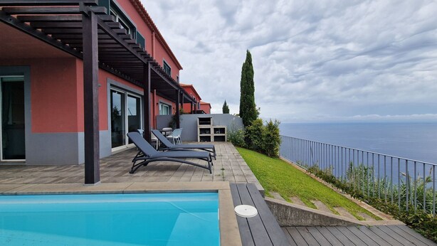 Un espace piscine avec des chaises longues, une pergola et une vue sur la mer.
