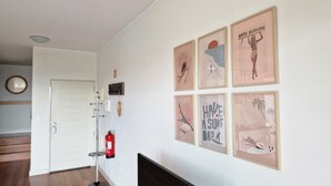 Un couloir avec un extincteur, un porte-manteau et des affiches encadrées accrochées au mur.