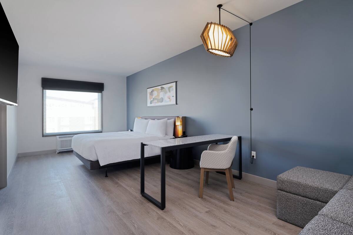 A modern bedroom with a bed, a desk, a chair, and a hanging light fixture.