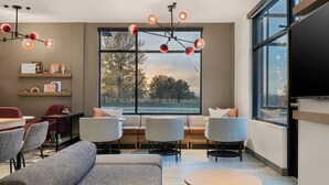 A modern living room with a large window, a sofa, chairs, a round table, and a TV. - Atwell Suites Kansas City Airport by IHG (Kansas City)