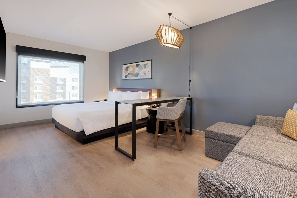 A modern bedroom with a bed, desk, chair, and a grey sofa.