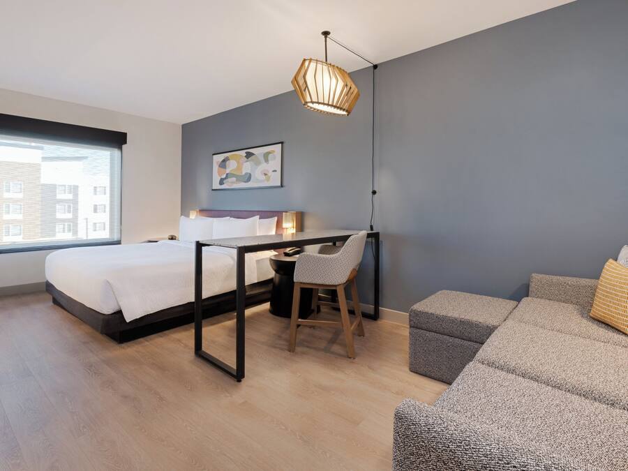 Un dormitorio moderno con cama, escritorio, silla y sofá gris.