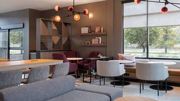 A modern interior with a long communal table, grey sofas, and red chairs.