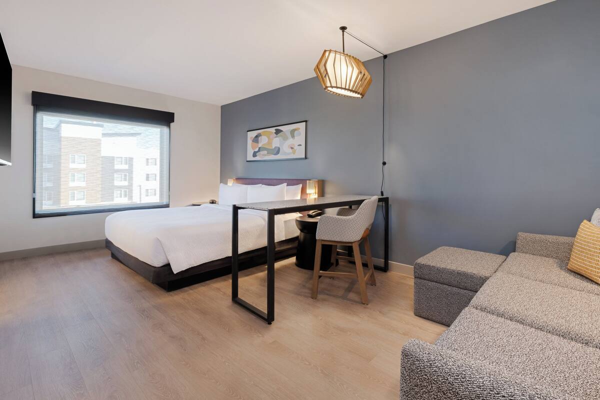 A modern bedroom with a bed, desk, chair, and a grey sofa.