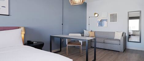 A modern hotel room with a bed, a desk, a sofa, and a large mirror.