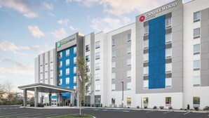 Un hotel Holiday Inn Express con un diseño moderno, que cuenta con una amplia pared azul de acento, una entrada techada y un estacionamiento.