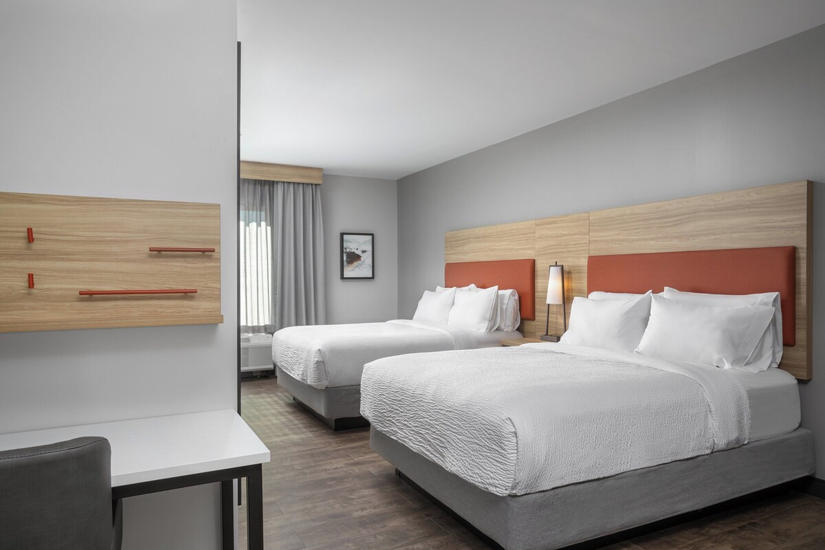 Habitación de hotel con dos camas, un escritorio y un amplio ventanal con cortinas.