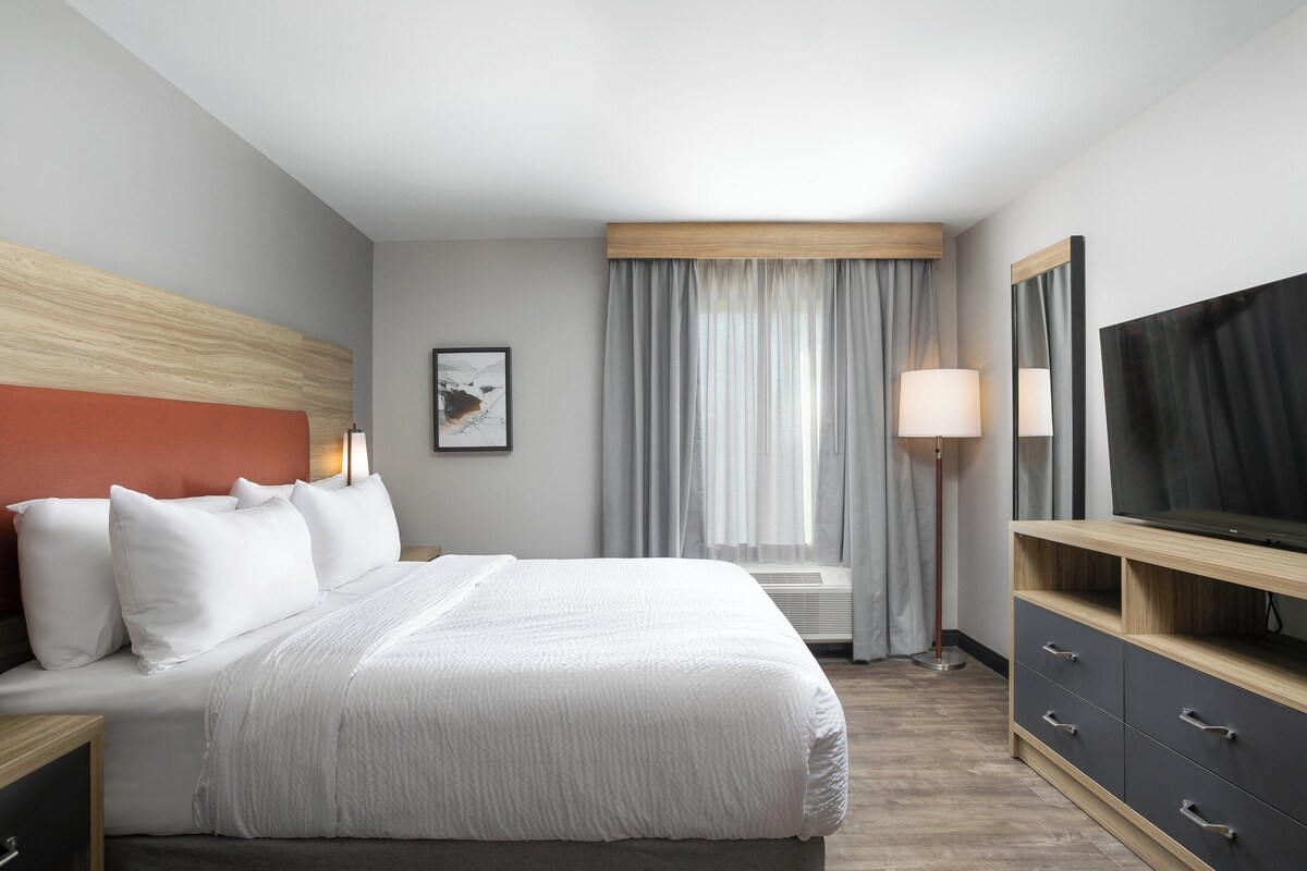Habitación de hotel con cama, televisión, escritorio y ventana con cortinas.