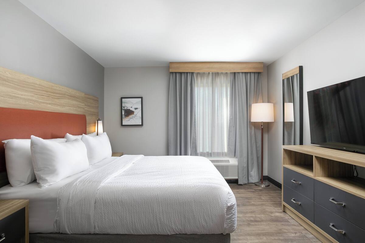 Hotellihuone, jossa on sänky, televisio, työpöytä ja ikkuna, jossa on verhot.