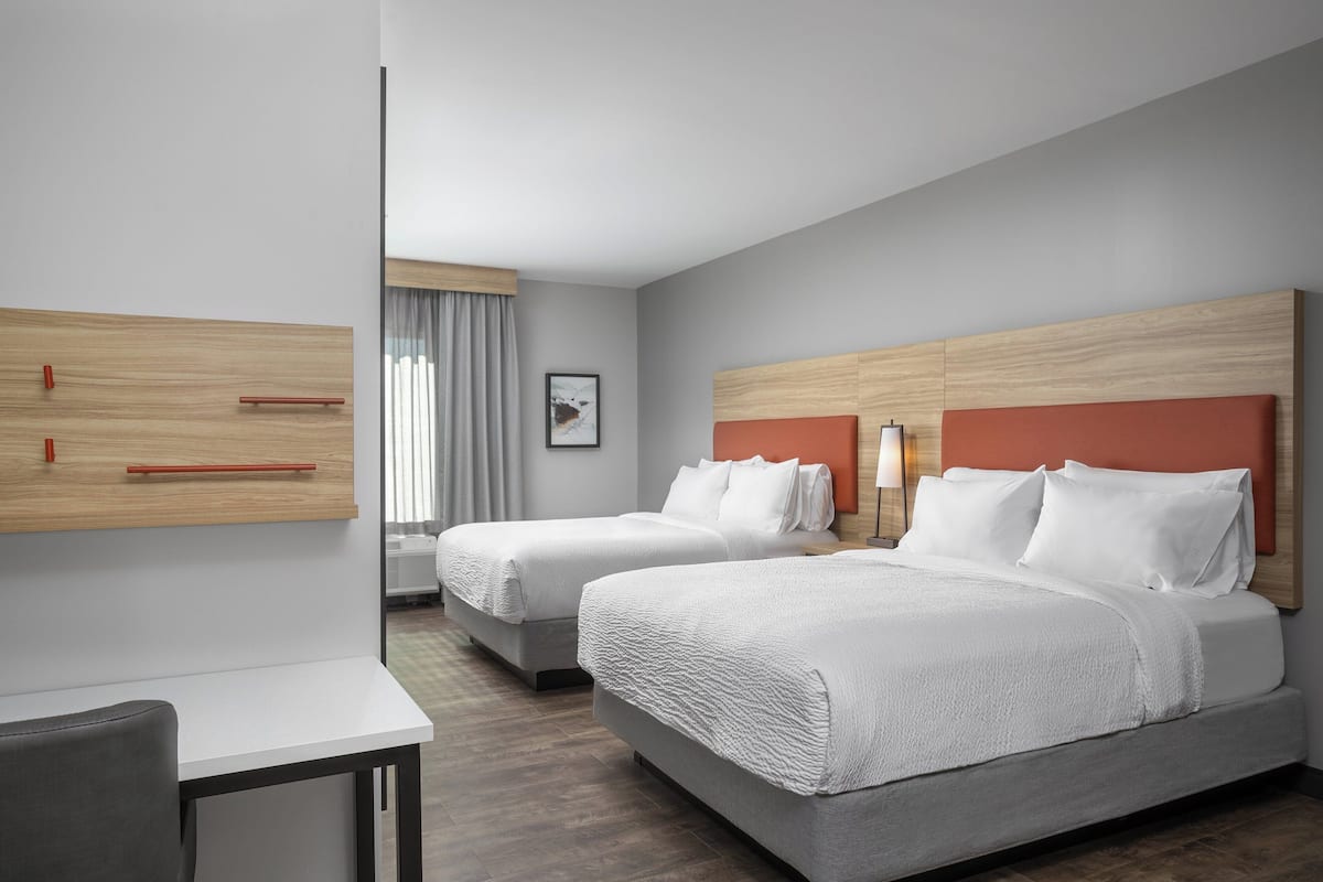 Hotellihuone, jossa on kaksi sänkyä, työpöytä ja suuri ikkuna, jossa on verhot.