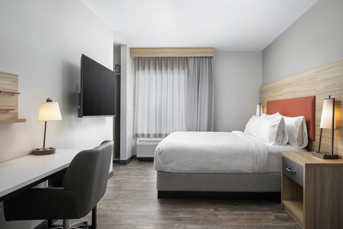 Hotellihuone, jossa on sänky, työpöytä, tuoli, televisio ja ikkuna, jossa on verhot.