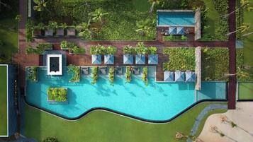 An aerial view of a resort with a large swimming pool, multiple lounge areas with umbrellas, and lush greenery surrounding the facilities.