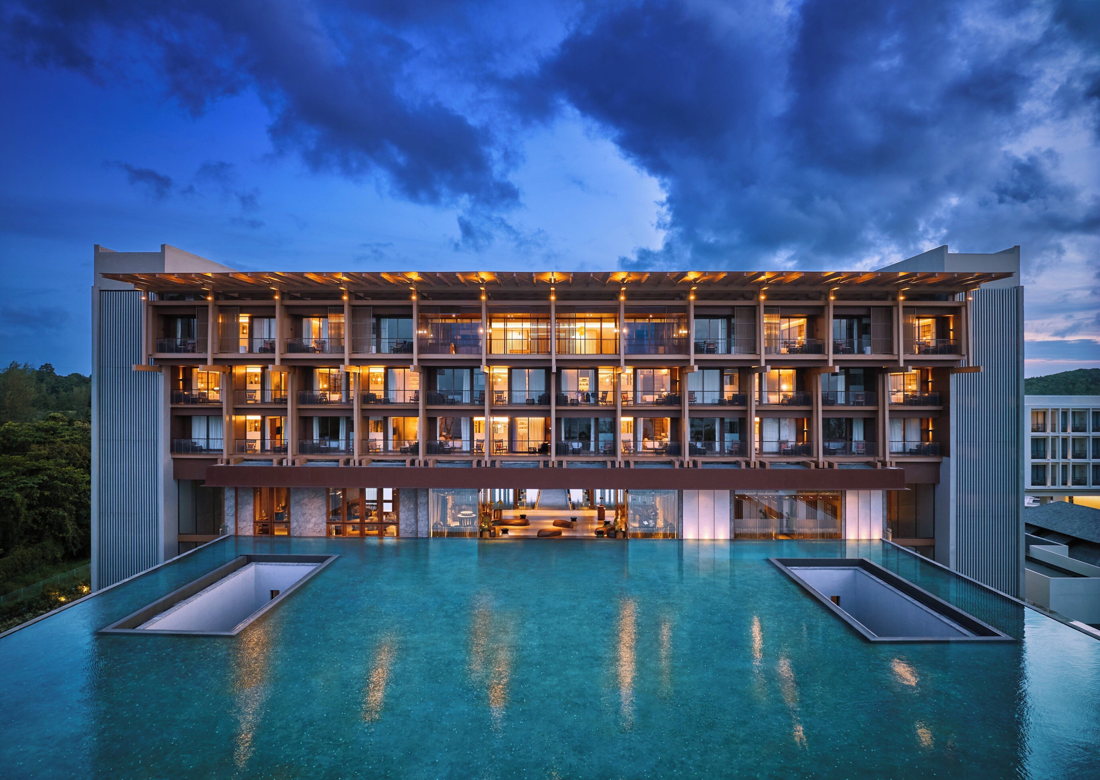 A modern hotel with multiple balconies, a rooftop pool, and a well-lit facade.