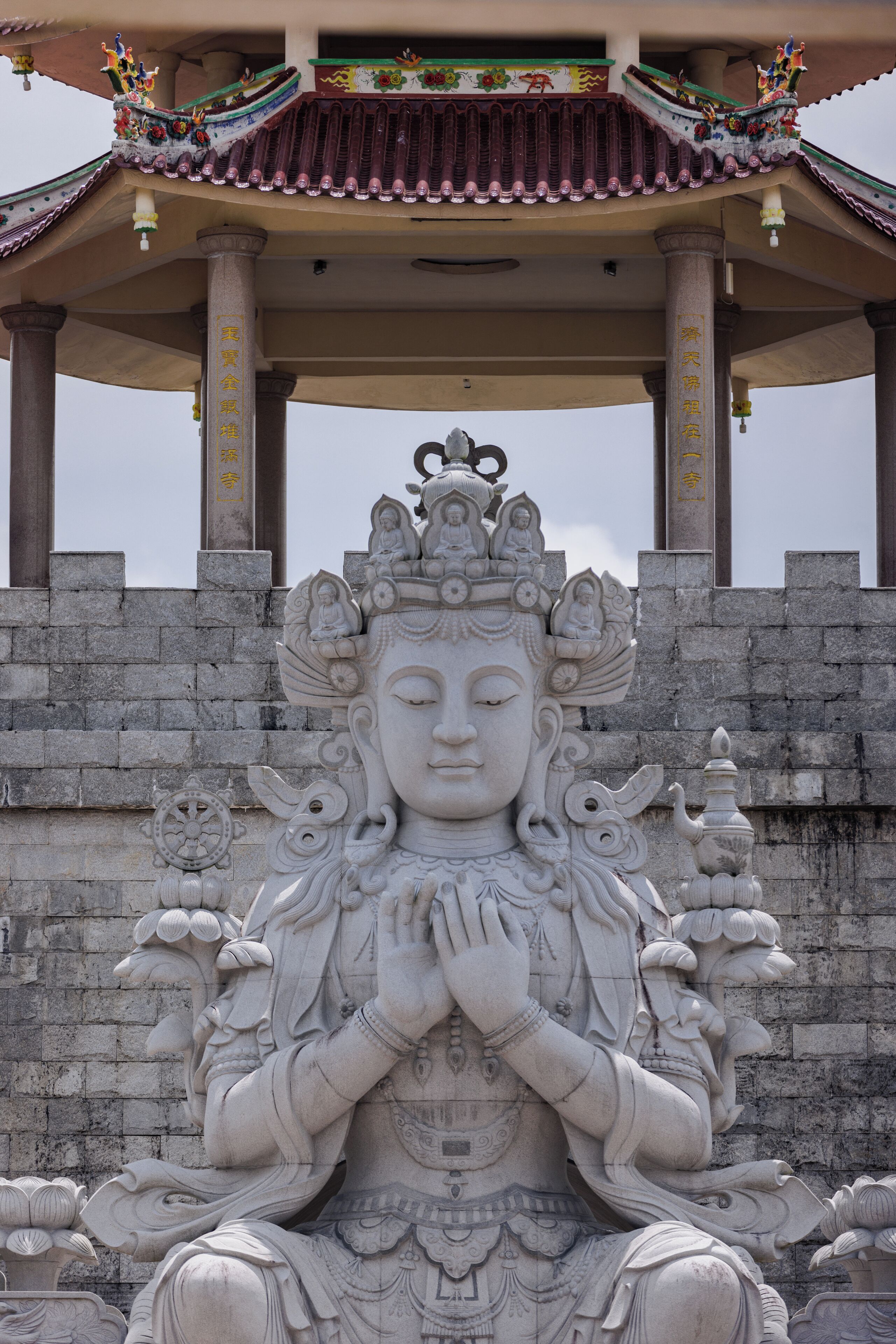 A stone statue of a deity with intricate carvings, set against a stone wall with traditional architectural elements.