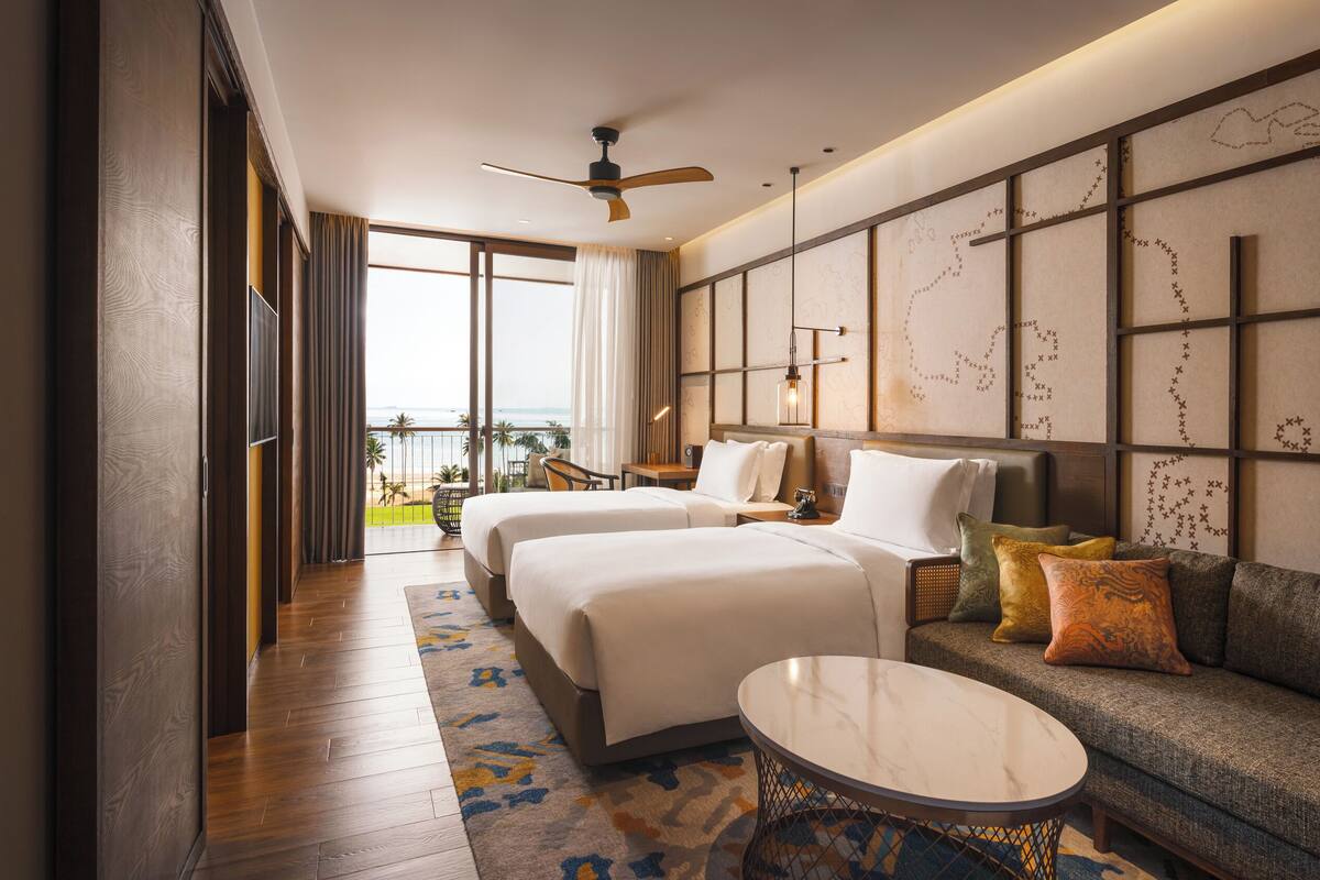 Ein Hotelzimmer mit zwei Betten, einem Sofa, einem мраморнем Couchtisch und Blick auf den Strand.