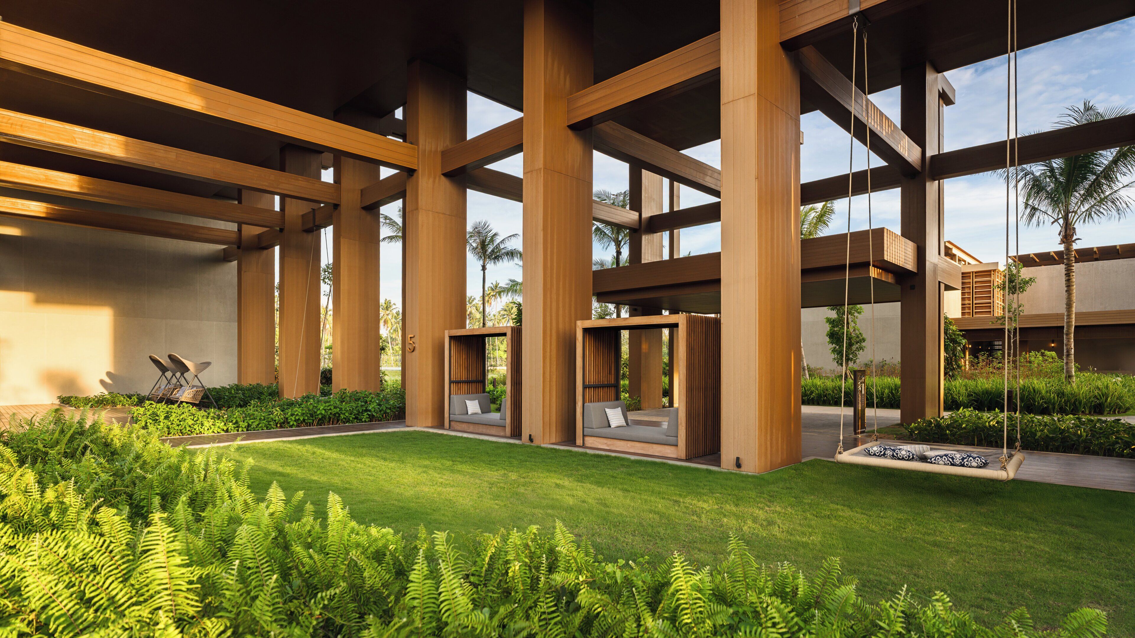 Una estructura arquitectónica moderna con grandes vigas de madera, zonas de estar al aire libre e exuberante vegetación.