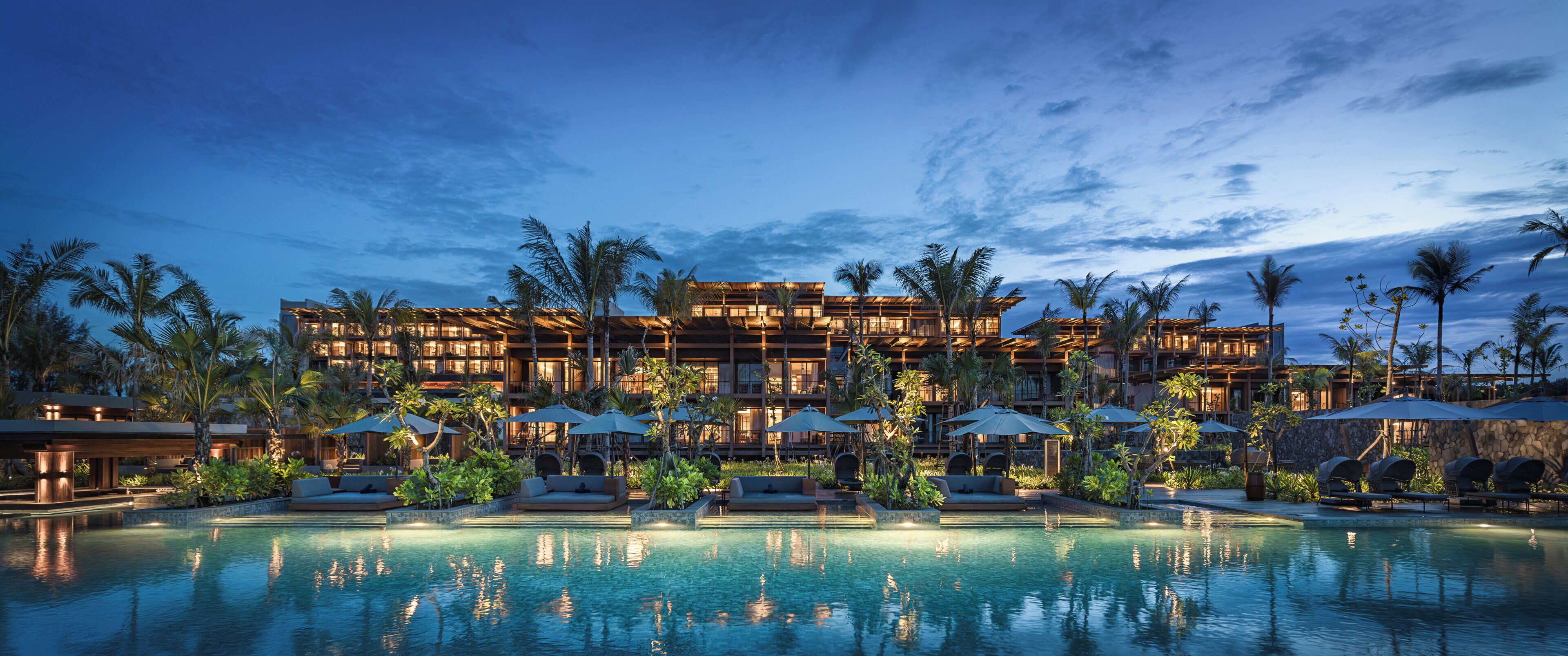 A resort with a large pool, lounge areas, and a multi-story building with outdoor seating and umbrellas.