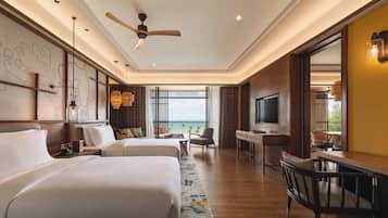 A hotel room with two beds, a desk, a chair, a TV, and a view of the sea.
