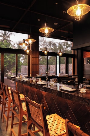 A bar area with wooden chairs, a long counter, and hanging pendant lights. - Hotel Indigo Bintan Lagoi Beach by IHG (Bintan)
