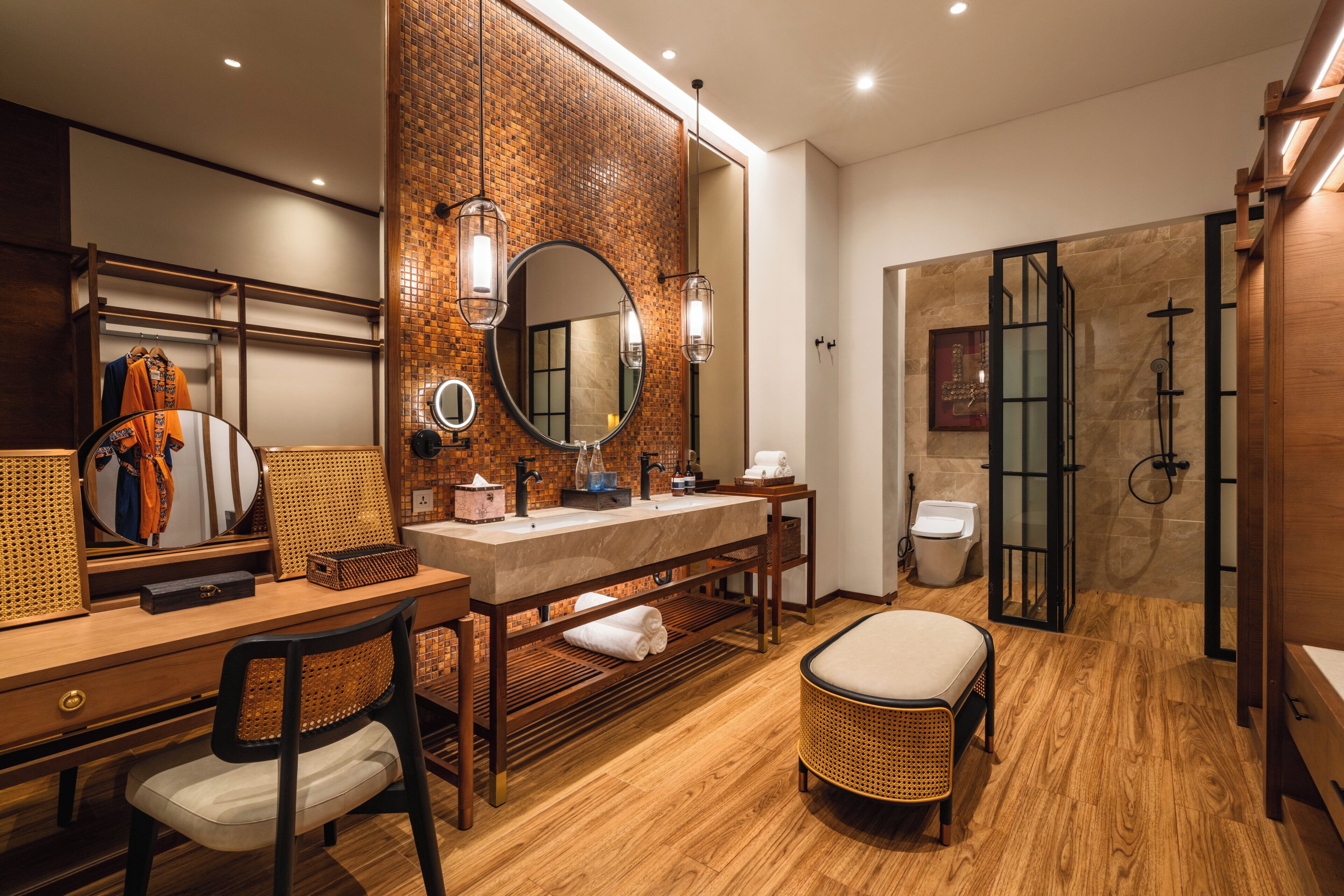 A modern bathroom with a wooden vanity, a round mirror, a shower area, and a seating area.