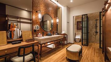 A modern bathroom with a wooden vanity, a round mirror, a shower area, and a seating area.