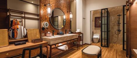 A modern bathroom with a wooden vanity, a round mirror, a shower area, and a seating area.