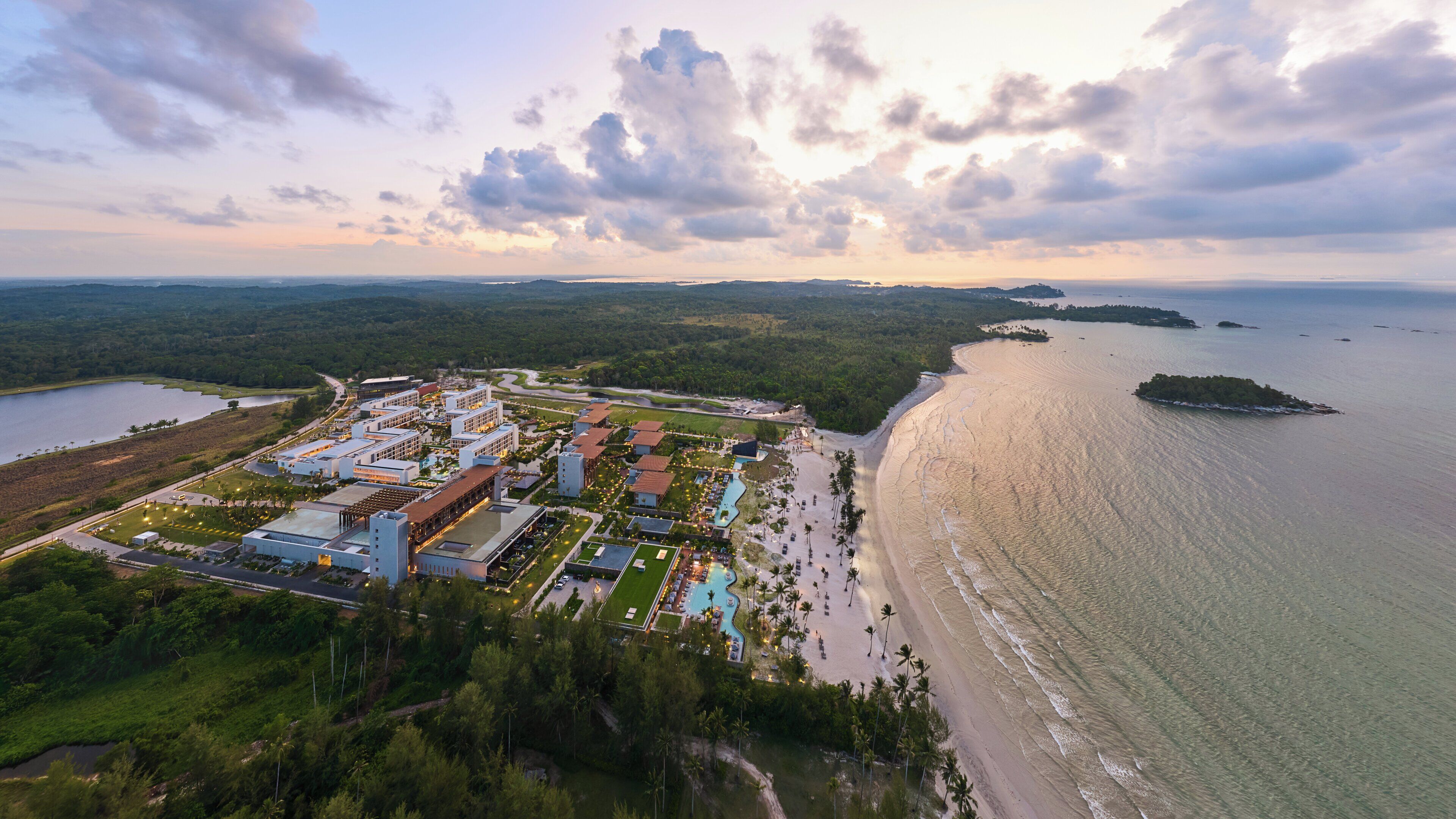 An aerial view of a coastal resort with multiple buildings, a beachfront, and a large body of water.