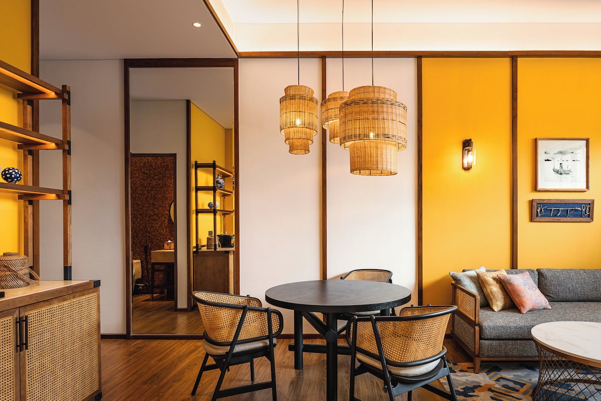 A modern living room with a sofa, a round table, wicker chairs, and a coffee machine.