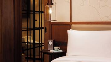 A hotel room with a bed, a small table with a clock and a cup, a wooden door, and a wall with a map design.