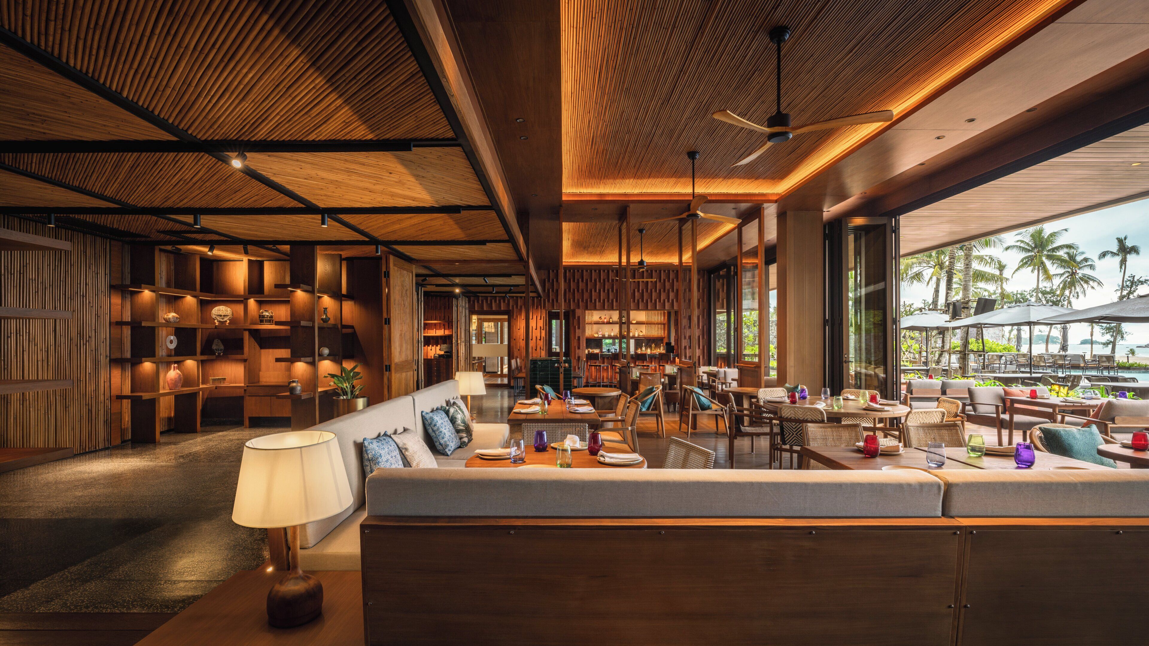 A modern hotel lobby with a wooden reception desk, seating area, and large windows offering a view of the ocean.