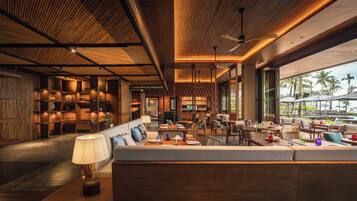 A modern hotel lobby with a wooden reception desk, seating area, and large windows offering a view of the ocean.