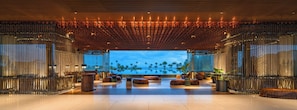 A spacious lobby with a view of the ocean, featuring a modern design with a wooden ceiling and metal railings.